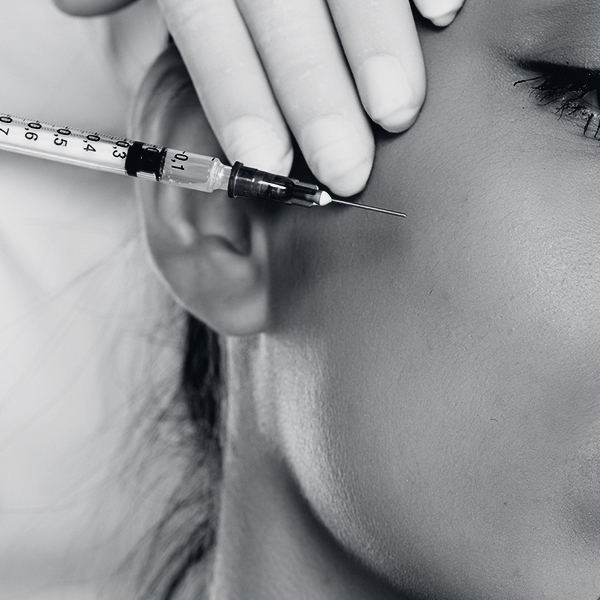 Portrait of a young beautiful woman with mobile phone on a face filler injection procedure on white background