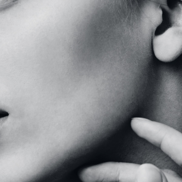 Close up portrait of young female brunette student girl with bun hairstyle and baked shoulders looking aside with calm face expression touching jawline with fingers. Beauty and health.